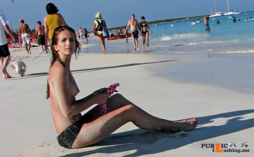 Teen brunette is sitting in the sand topless